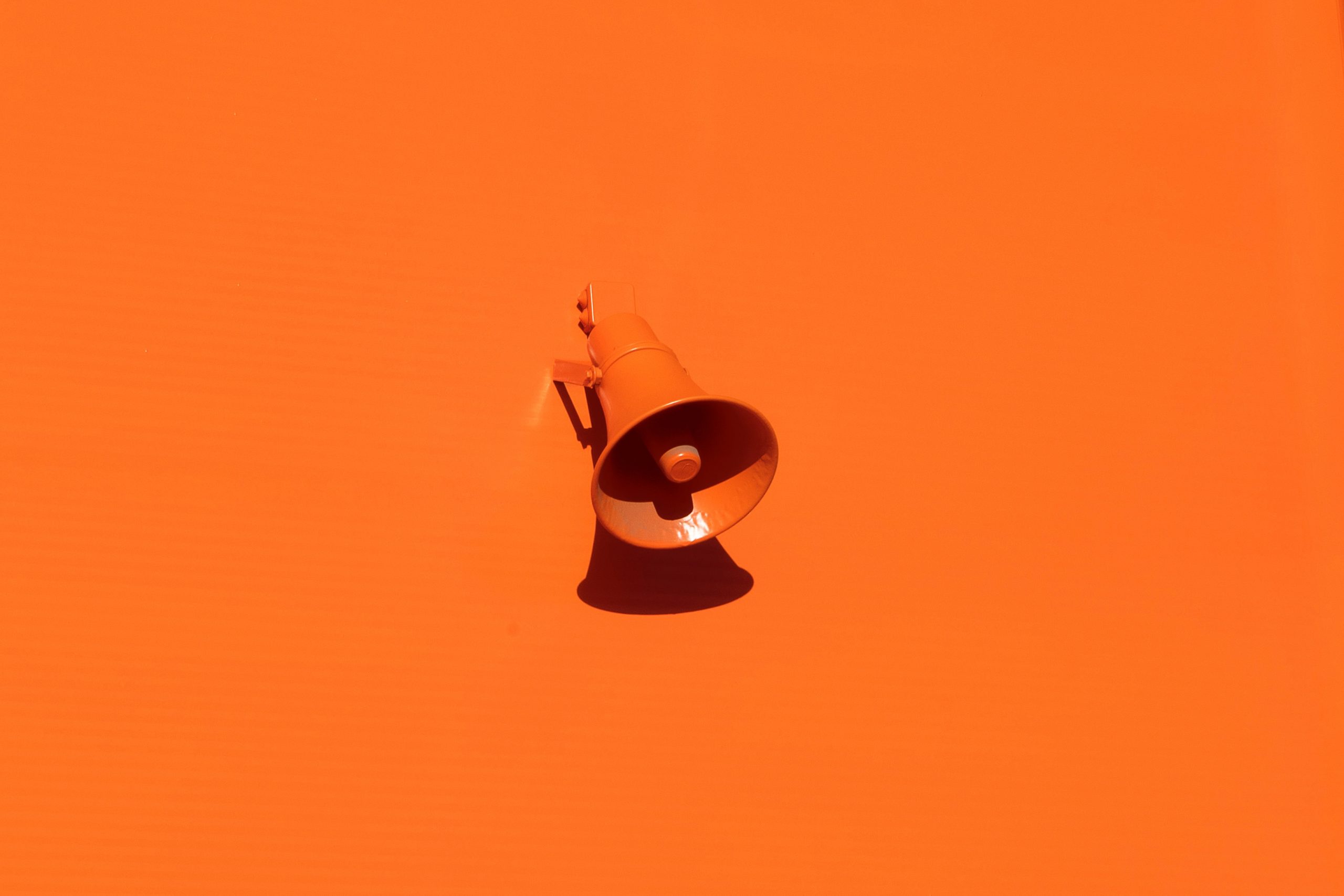 Parede laranja com um megafone, também laranja, e sombra projetada para baixo, simbolizando a comunicação.