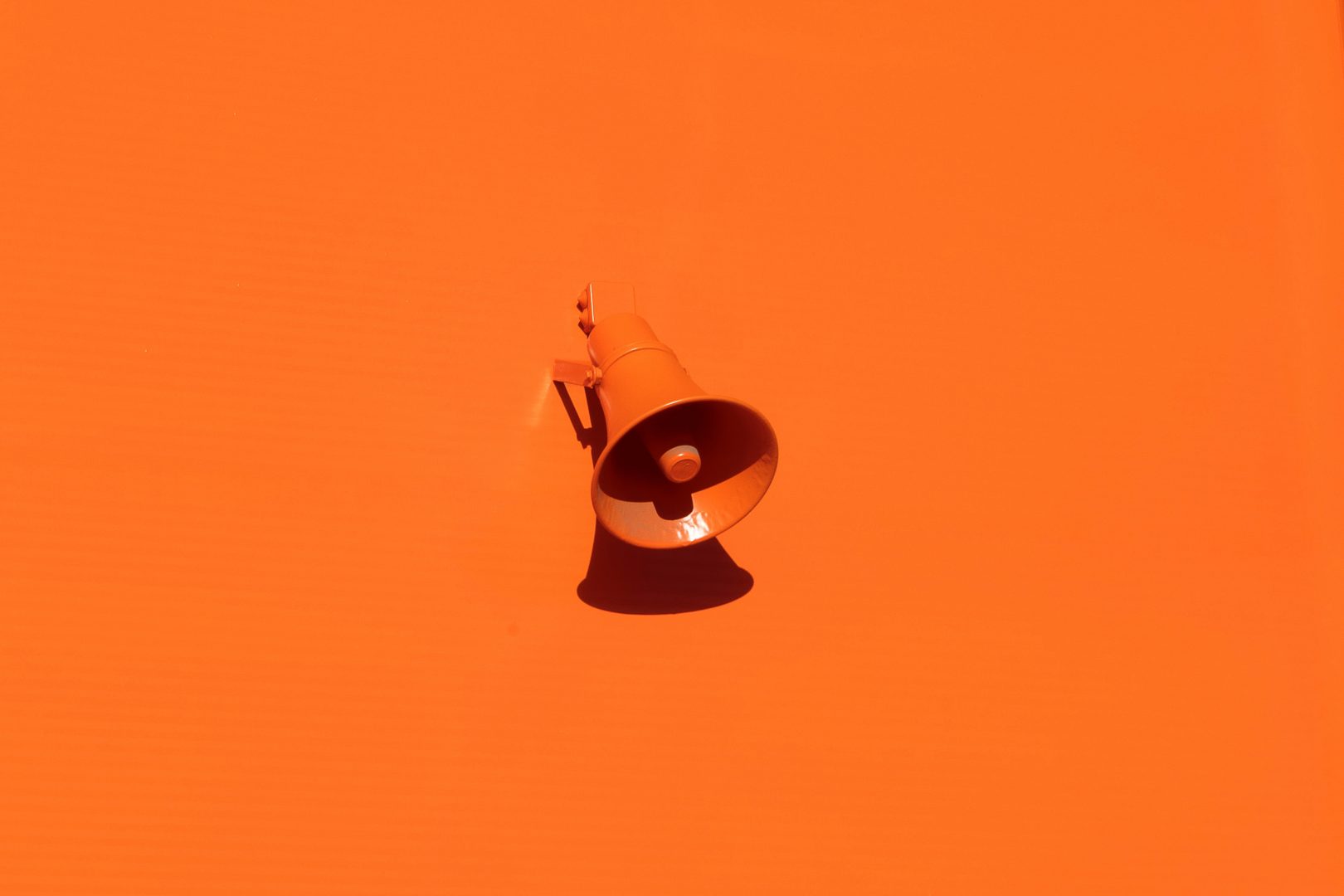 Parede laranja com um megafone, também laranja, e sombra projetada para baixo, simbolizando a comunicação. 